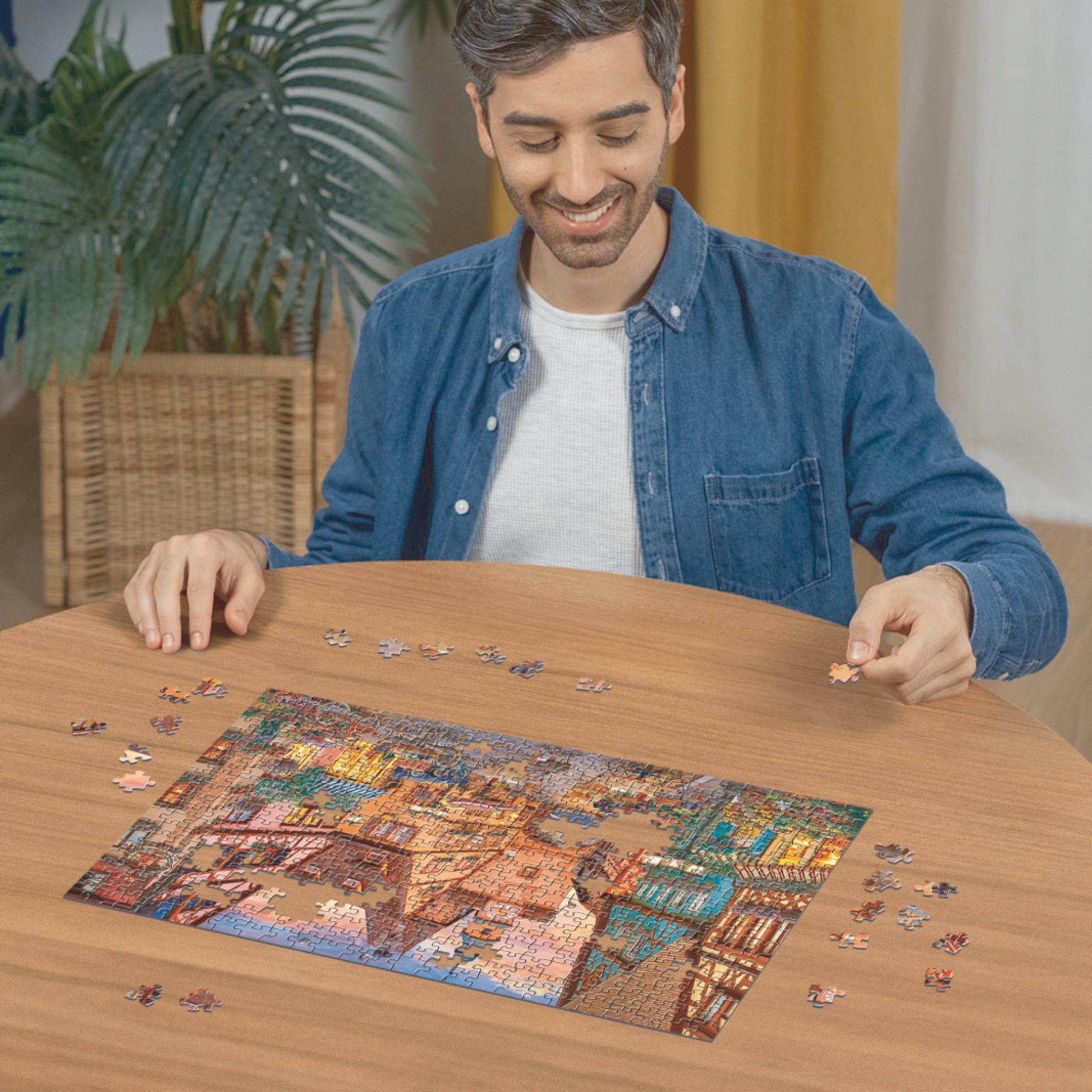 Person pusler Ravensburger puslespill ved trebord med puslespillbrikker spredt rundt